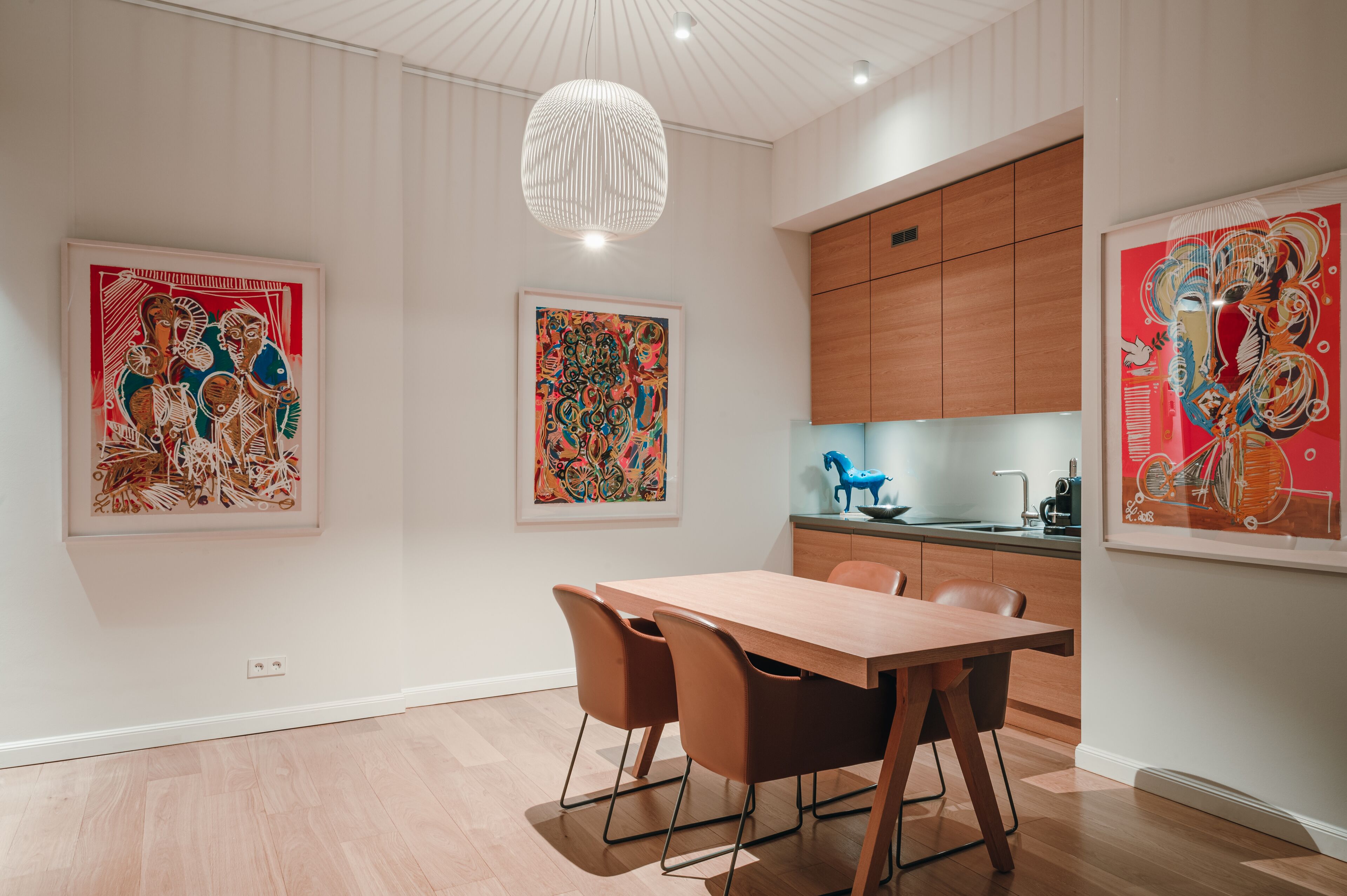 Un'area pranzo moderna con un tavolo e sedie in legno, circondata da opere d'arte astratte e colorate.