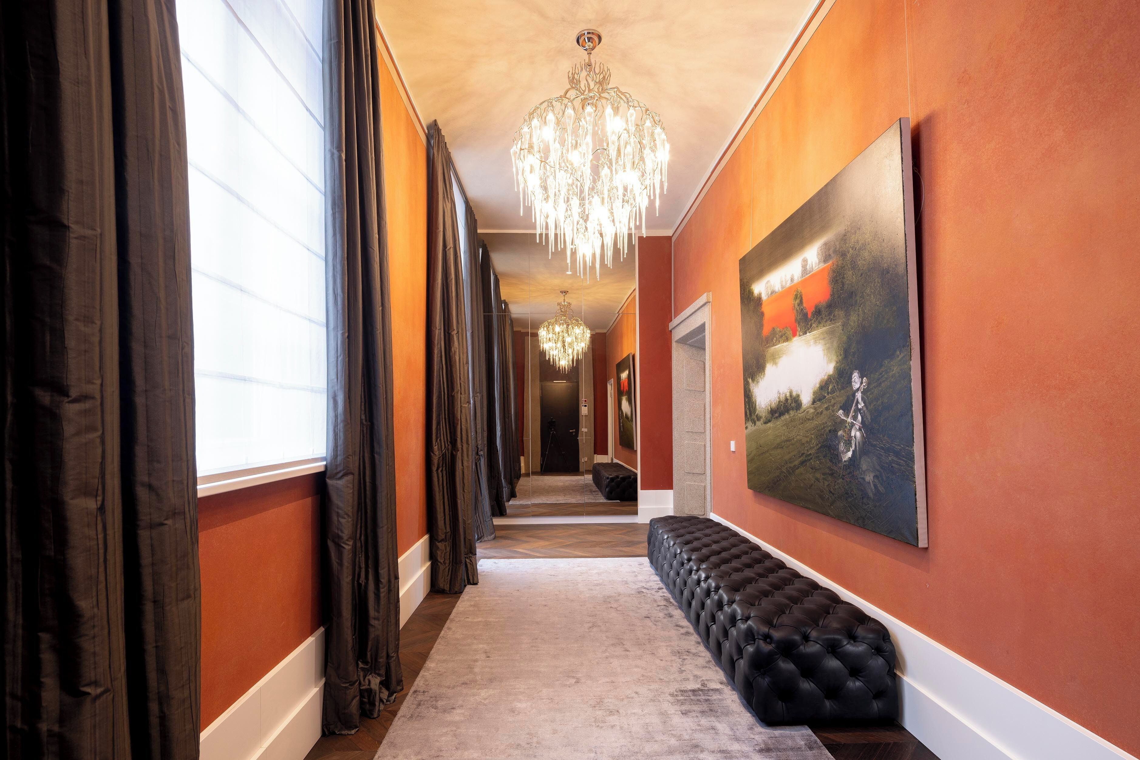 A hallway with a chandelier, a large painting, and a black bench.