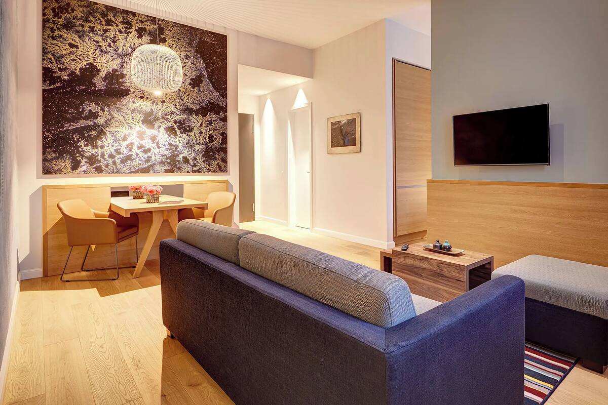 A modern hotel room with a sofa, a small table, a TV, and a bed.