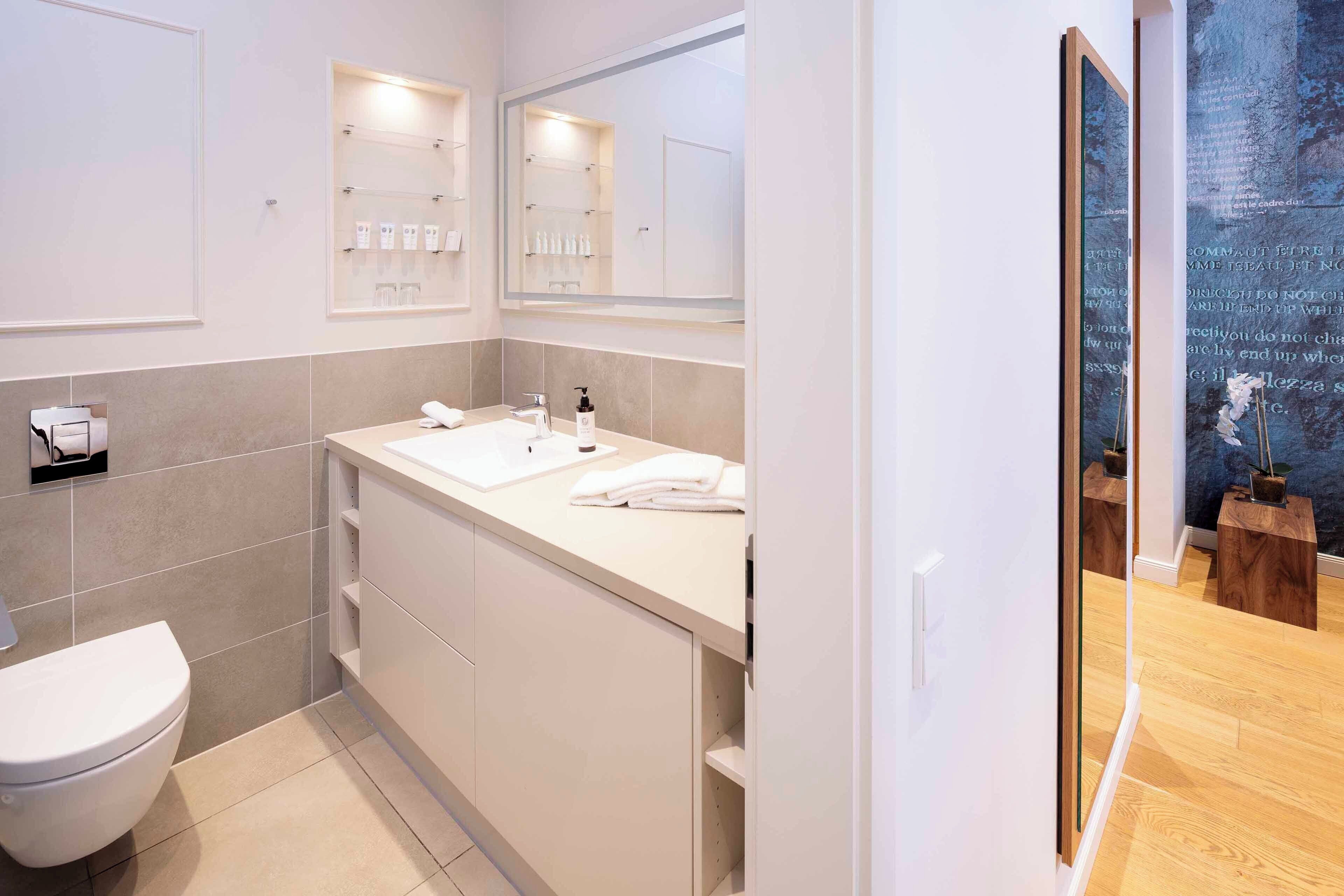 Un baño moderno con lavamanos, espejo y retrete blancos.