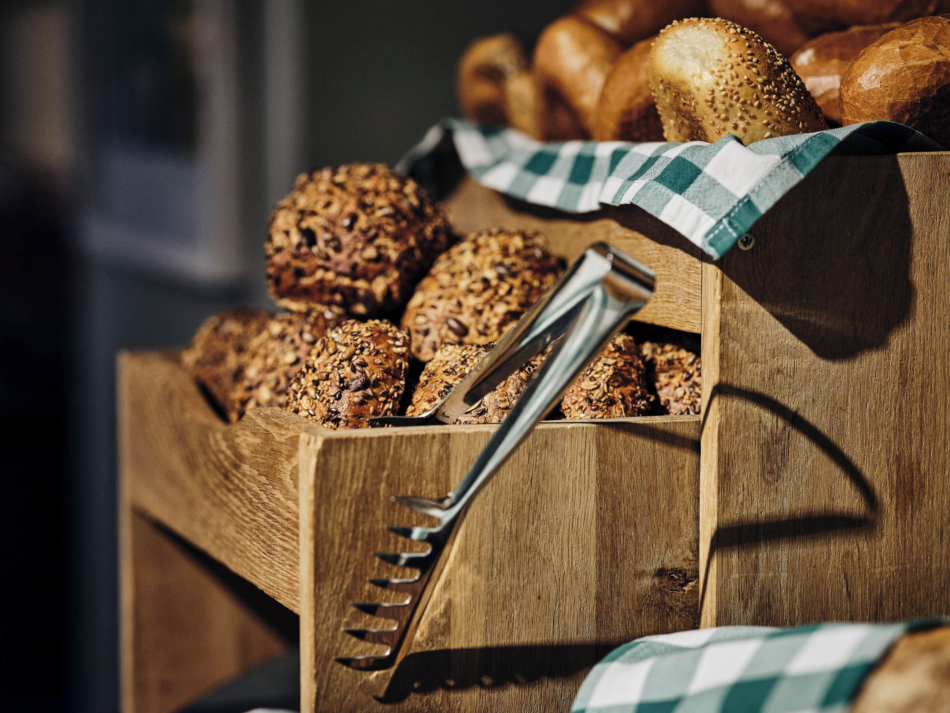 A wooden crate filled with various types of bread and a pair of tongs.