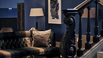 A dark blue room with a tufted sofa, a lamp, and a staircase.