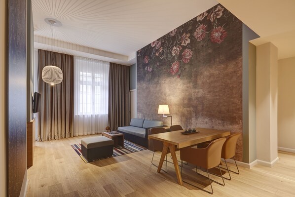 A modern living room with a sofa, a dining table, and a large floral mural on the wall.