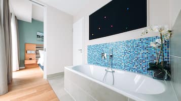 Un bagno moderno con una vasca da bagno ampia, un muro in mosaico blu e un'orchidea in vaso.