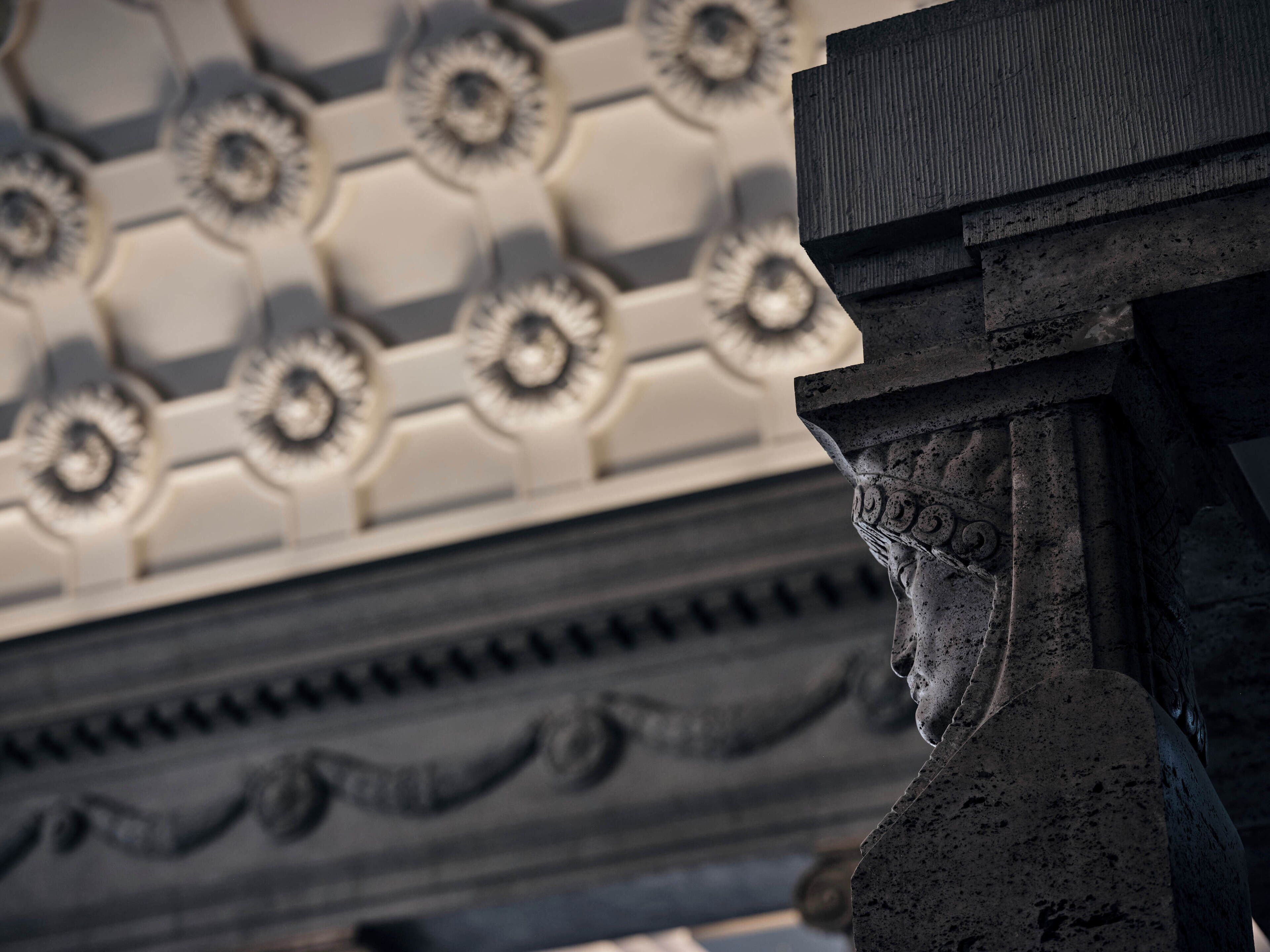 Primer plano de una columna arquitectónica clásica con intrincados grabados, parte de una estructura más grande con techo decorado.
