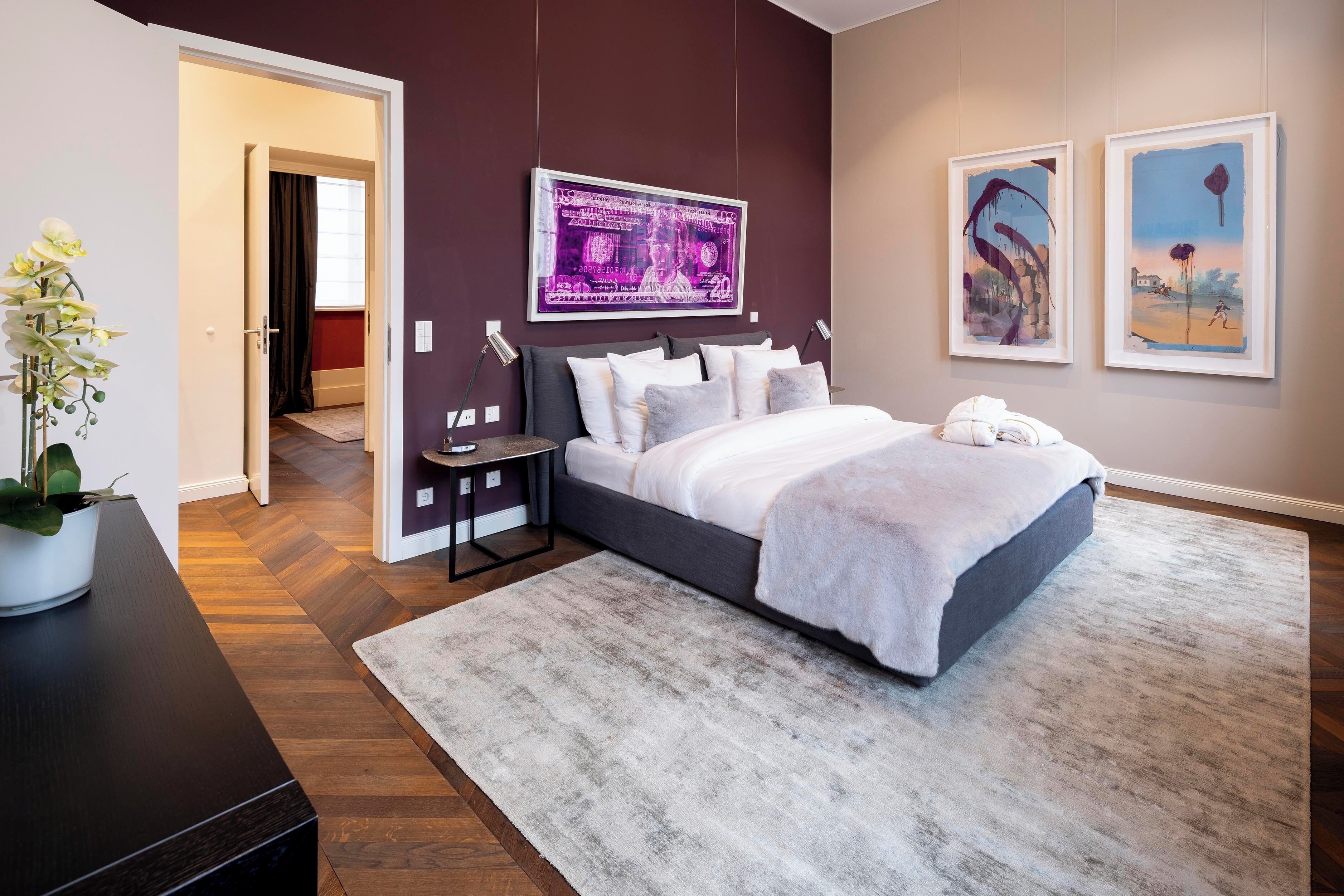 Ein modernes Schlafzimmer mit einem großen Bett, einem Nachttisch, einer Topfpflanze und Kunstwerken an den Wänden.