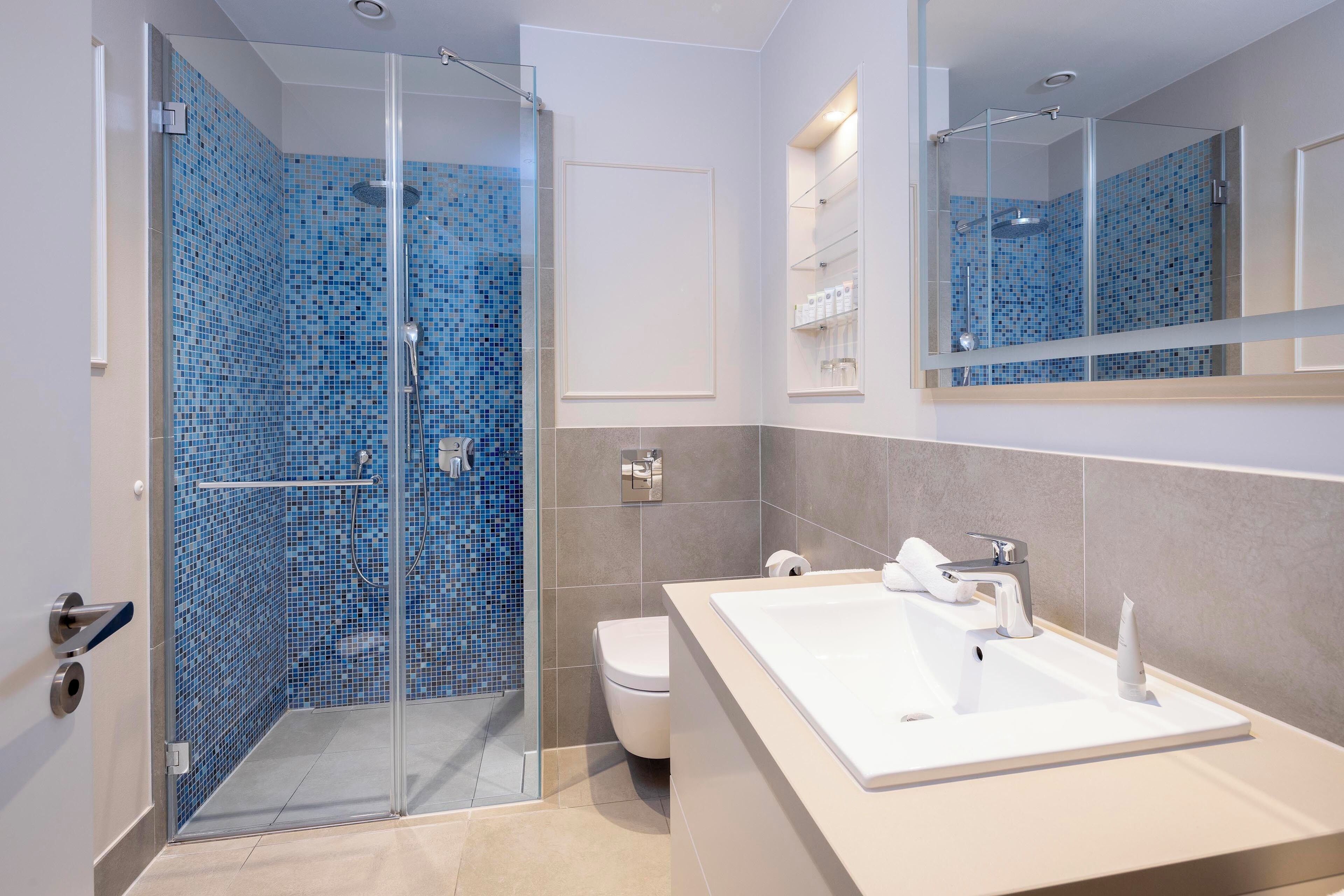 A modern bathroom with a glass-enclosed shower, a white sink, and a tiled shower area.