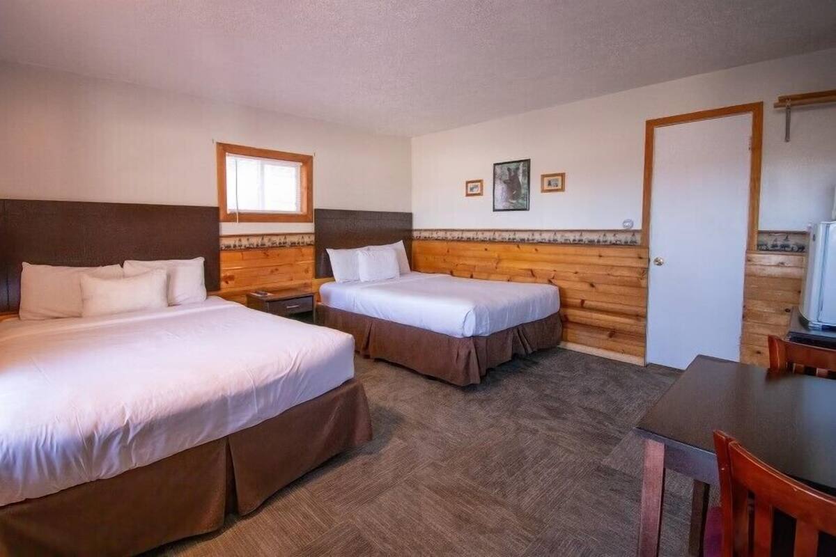 A room with two beds, wooden headboards, a small window, and a door.