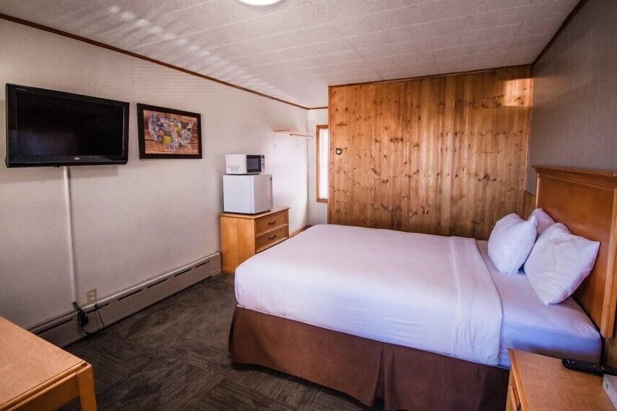 A hotel room with a bed, a television, a microwave, and a wooden headboard.