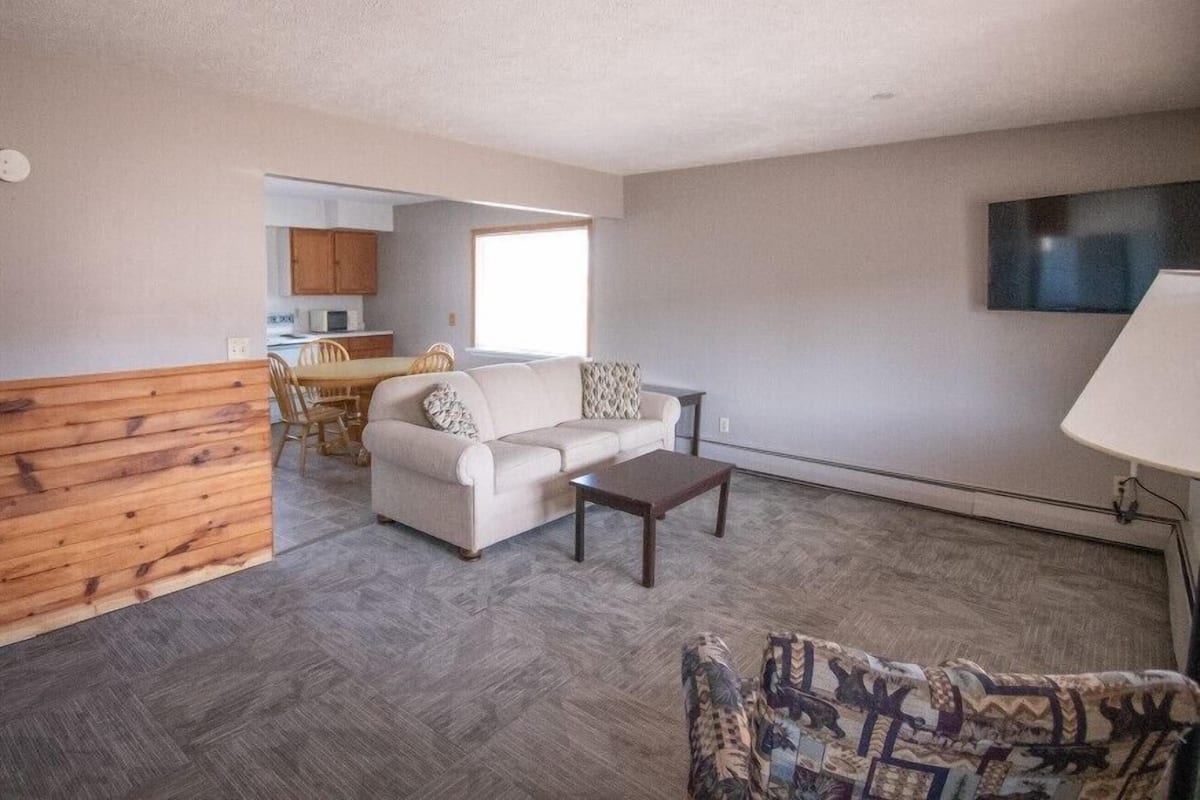 A living room with a sofa, coffee table, and patterned armchair. A TV is mounted on the wall.