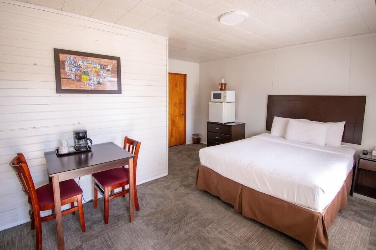 A hotel room with a bed, a desk with two chairs, a microwave, and a framed map on the wall.
