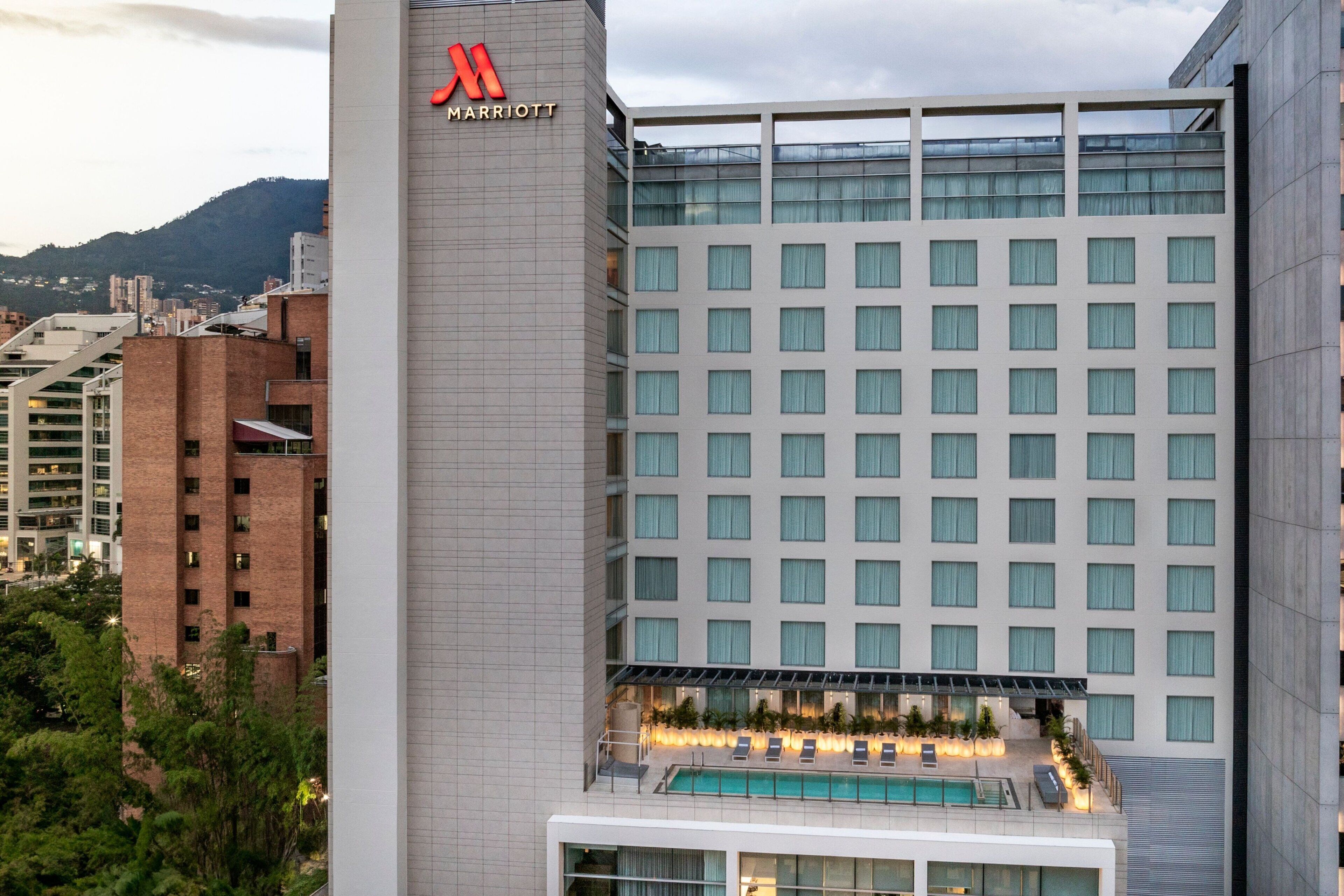 Un hôtel moderne arborant le logo Marriott, doté d’une piscine sur le toit et offrant une vue sur le paysage urbain environnant.