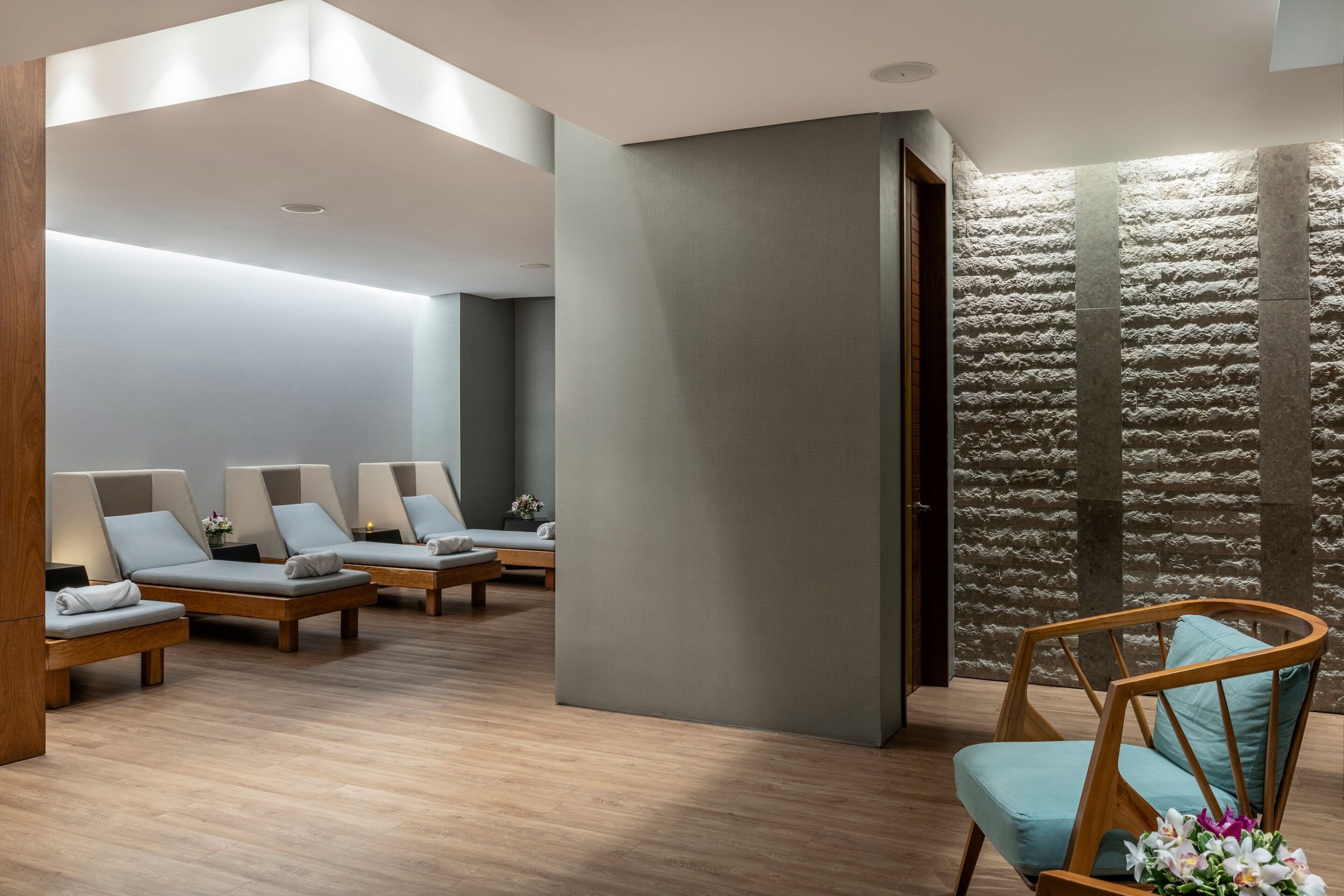 Un moderno cuarto de spa con suelo de madera, pared de piedra y una silla de madera con cojín.