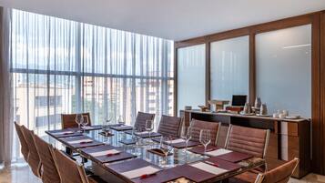 A modern conference room with a long table, leather chairs, and large windows offering a city view.