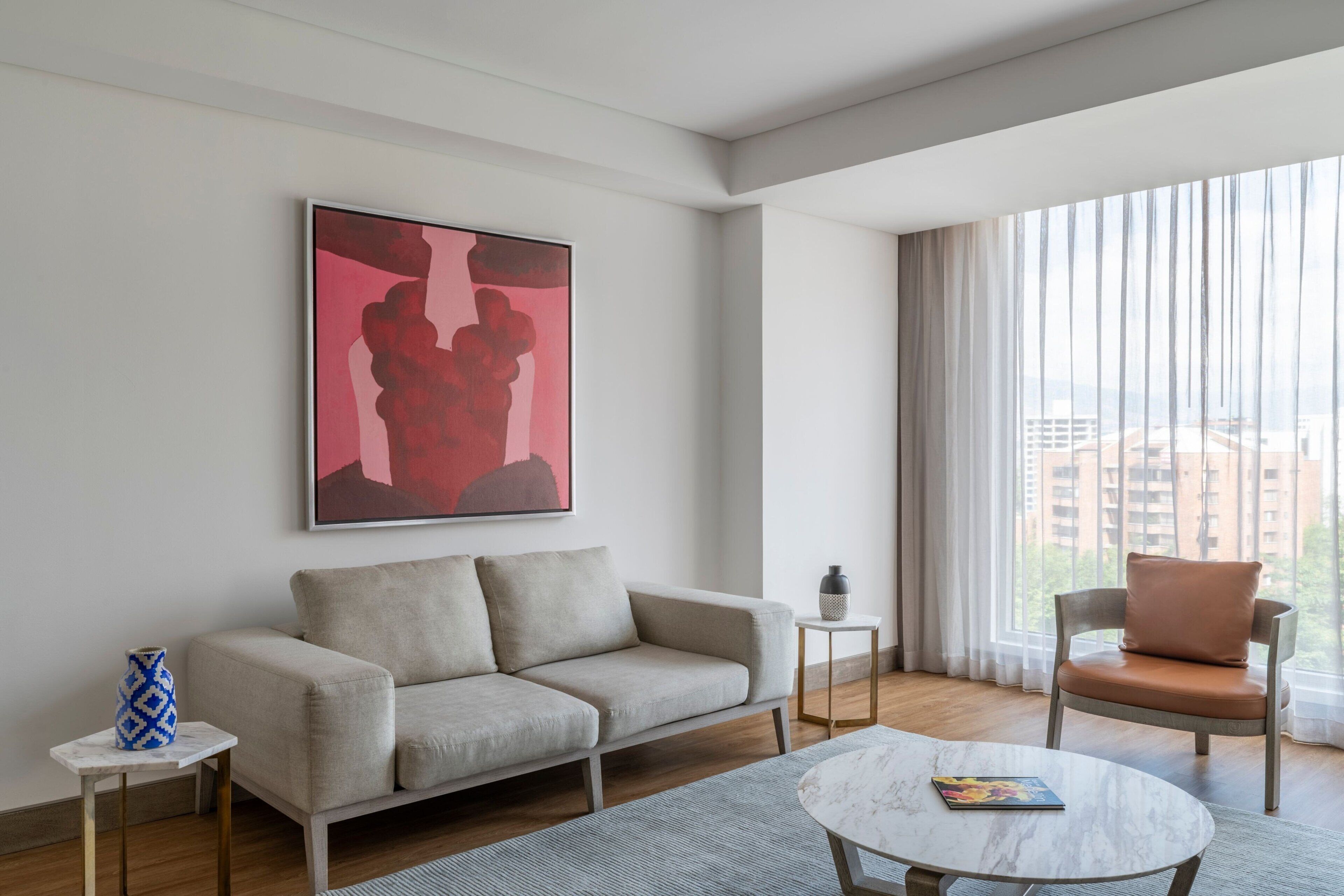A modern living room with a sofa, a round coffee table, a chair, and a large window with curtains.