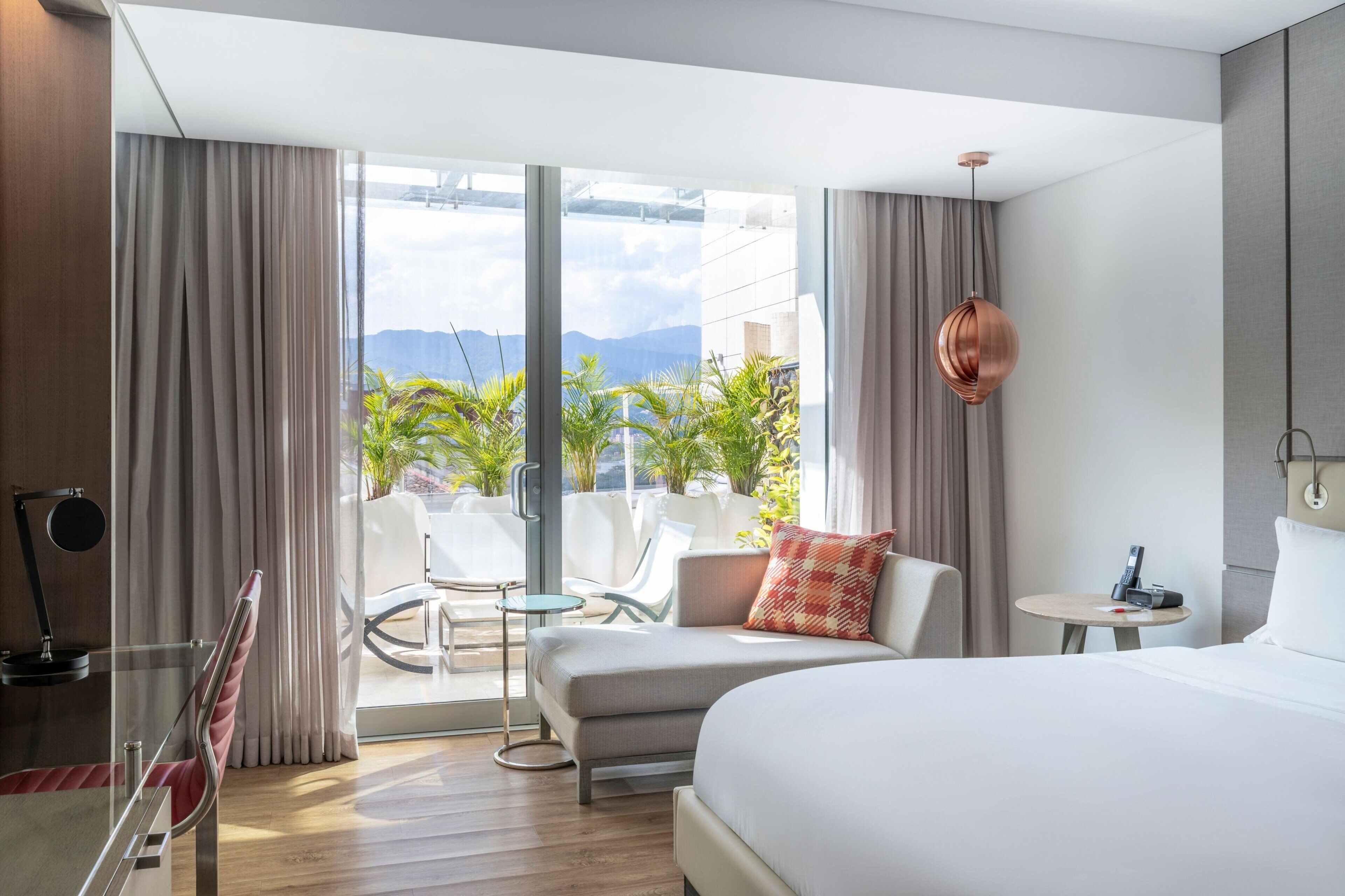 A hotel room with a bed, a sofa, a small table, a chair, and a view of the outdoors.