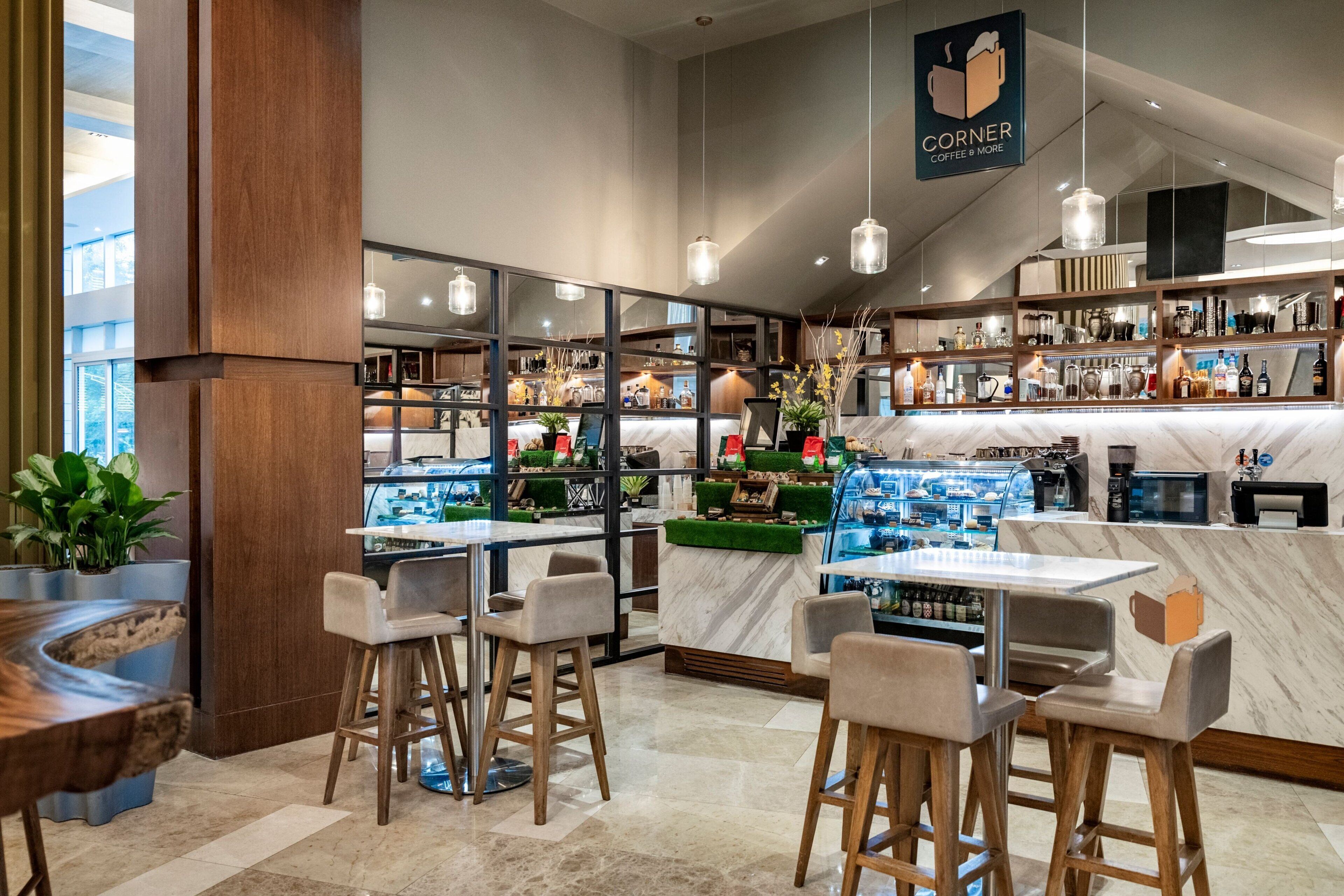 Un interno di caffetteria moderno, con sgabelli da bar, un bancone in marmo e diverse esposizioni di caffè e tè.
