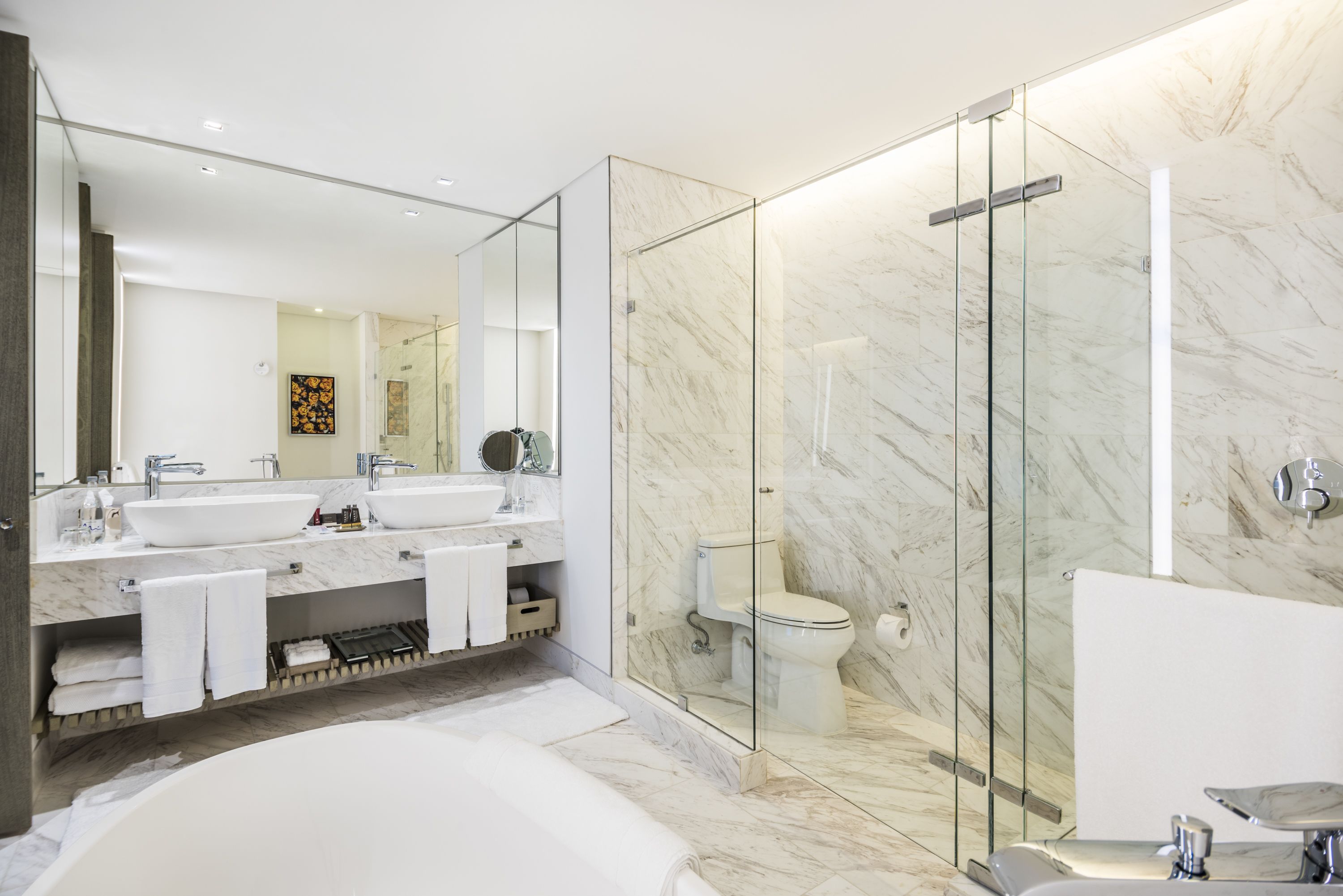 Un baño moderno con una bañera grande, dos lavamanos, una ducha con cerramiento de vidrio y paredes de mármol.