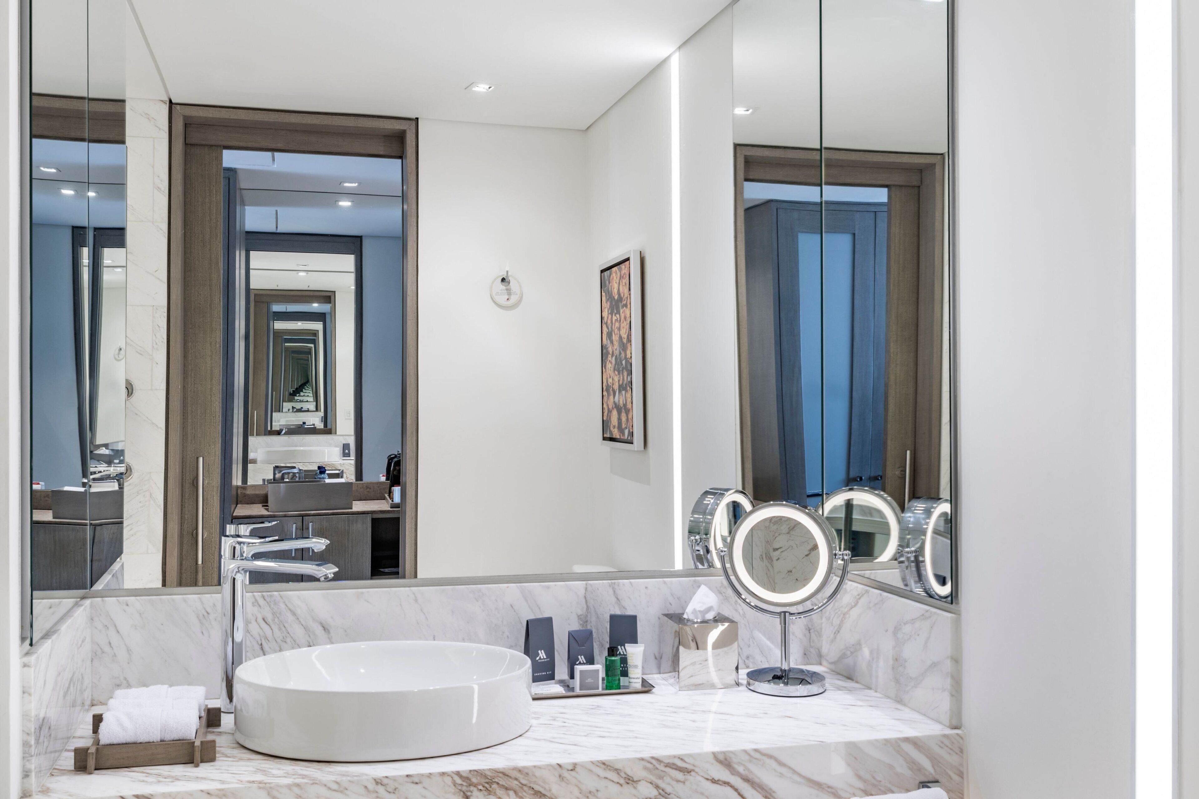 A modern bathroom with a large mirror, a round sink, and a marble countertop.