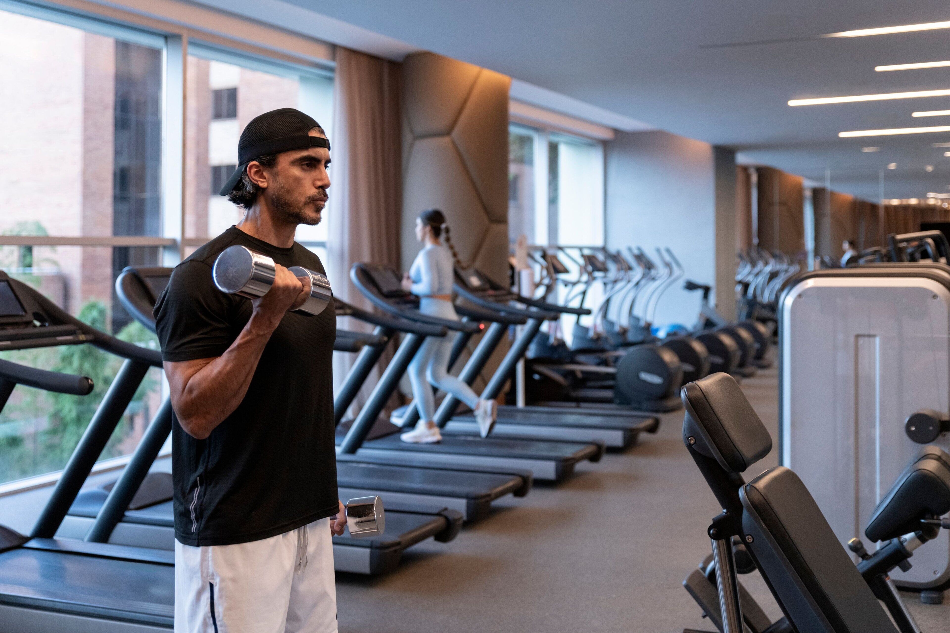 Un gimnasio con cintas de correr, máquinas de pesas y una persona usando mancuernas.