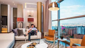 A modern hotel room with a large window offering a city view, a sofa, a coffee table, and a laptop.