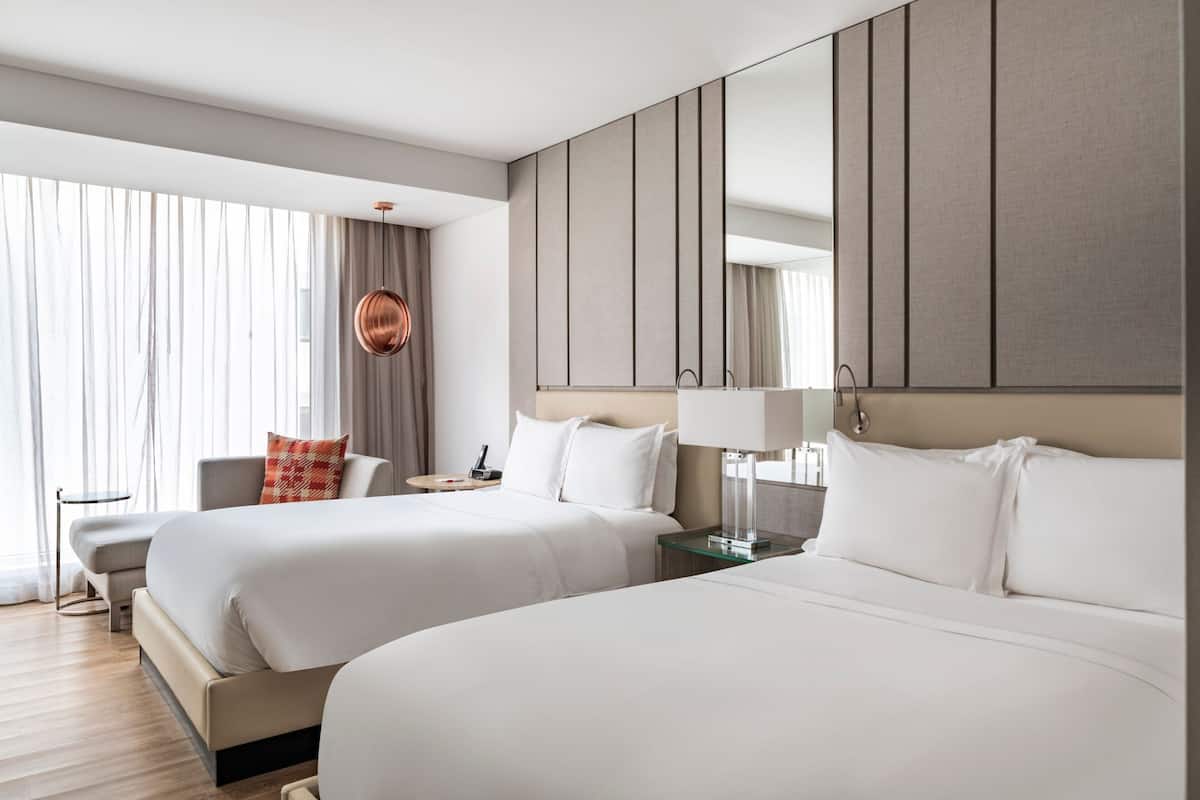 Une chambre d’hôtel moderne avec deux lits, un grand miroir et une vue sur l’extérieur.