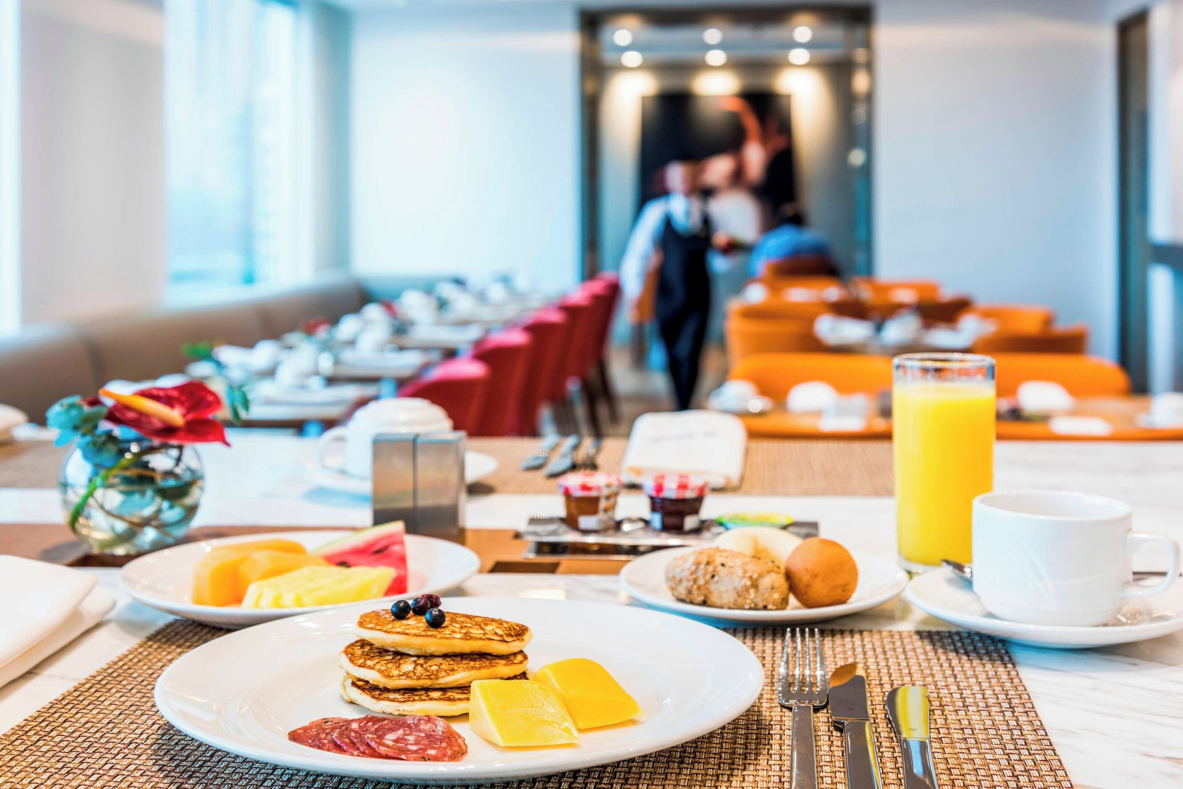 A breakfast buffet with plates of pancakes, toast, and pastries, along with a glass of orange juice.