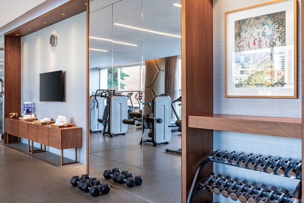 Un gimnasio con equipo de ejercicio, un espejo grande y un estante con mancuernas.