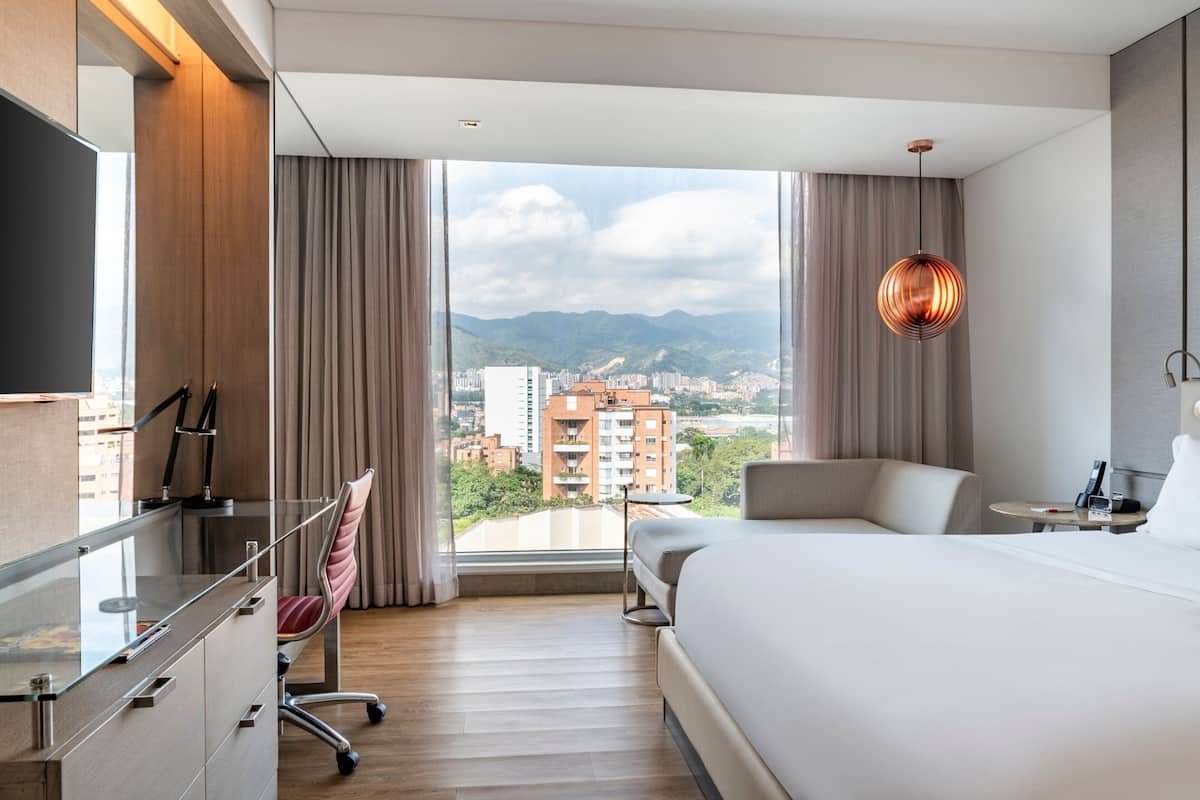 Une chambre d’hôtel moderne dotée d’un grand lit, d’un bureau et offrant une vue sur le paysage urbain.