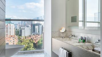 A modern bathroom with a large window, a bathtub, a vanity with a mirror, and a towel rack.