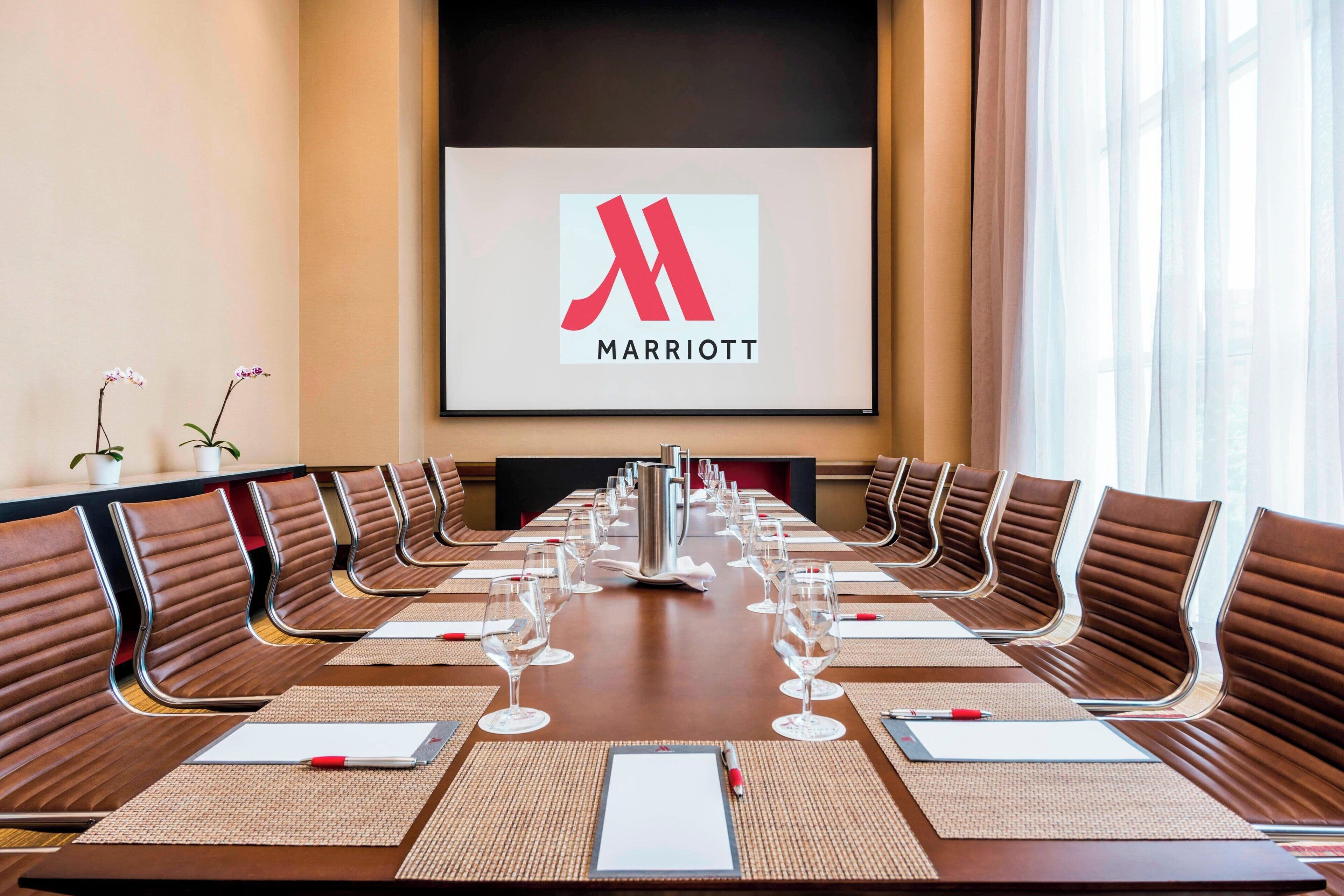 Ein Konferenzraum mit einem langen Tisch, braunen Ledersesseln und einem großen Bildschirm, der das Marriott-Logo zeigt.