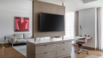 A modern living room with a large flat-screen TV mounted on a wooden wall, a grey sofa, a small side table with a vase, and a red office chair.
