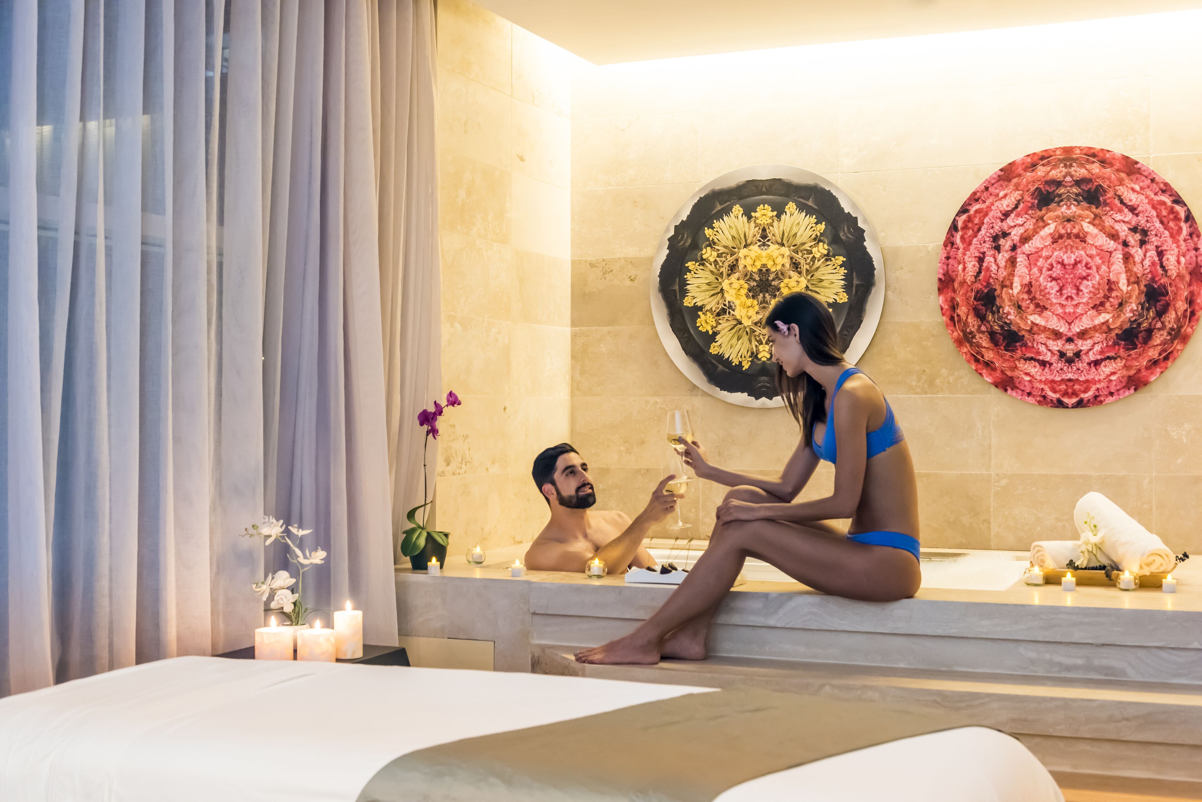 A couple in a bathtub with candles and a flower arrangement.
