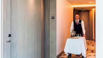 Un couloir d’hôtel avec une porte en bois portant l’inscription « 1003 », une table blanche sur laquelle se trouve un plateau avec de la nourriture et des boissons, et un sol recouvert de moquette.