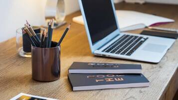A wooden desk with a laptop, a cup of pencils, a book titled "Room Key," and a magazine.