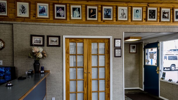A reception area with a wooden reception desk, framed pictures on the wall, and a large wooden door with glass panels. - Lakeview Lodge Motel (Lakeview)