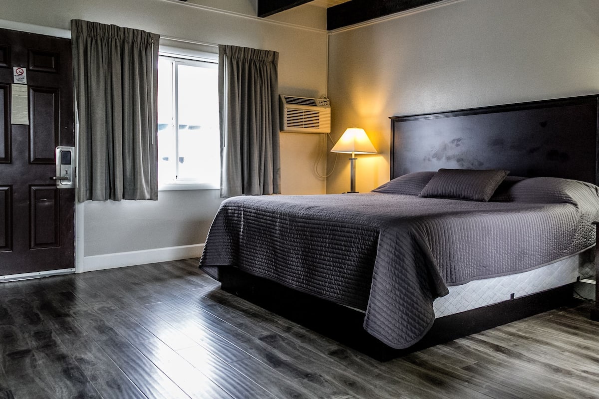 A modern hotel room with a large bed, a bedside lamp, and a window with curtains.