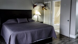 A neatly made bed with a dark headboard, a bedside lamp, and a hanging coat rack. - Lakeview Lodge Motel (Lakeview)