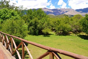 A wooden deck with a view of a grassy field and mountains in the background. - Cabañas El Algodonal (Nono)