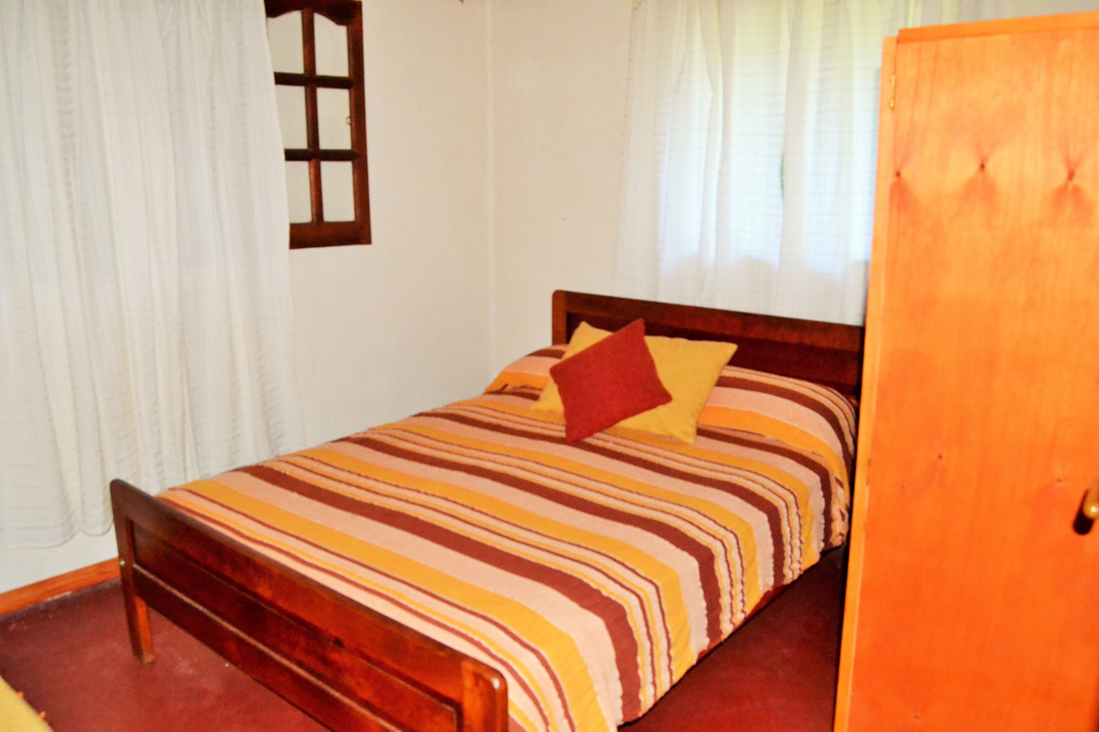Een kamer met een houten bed, gestreept beddengoed en een houten kledingkast.