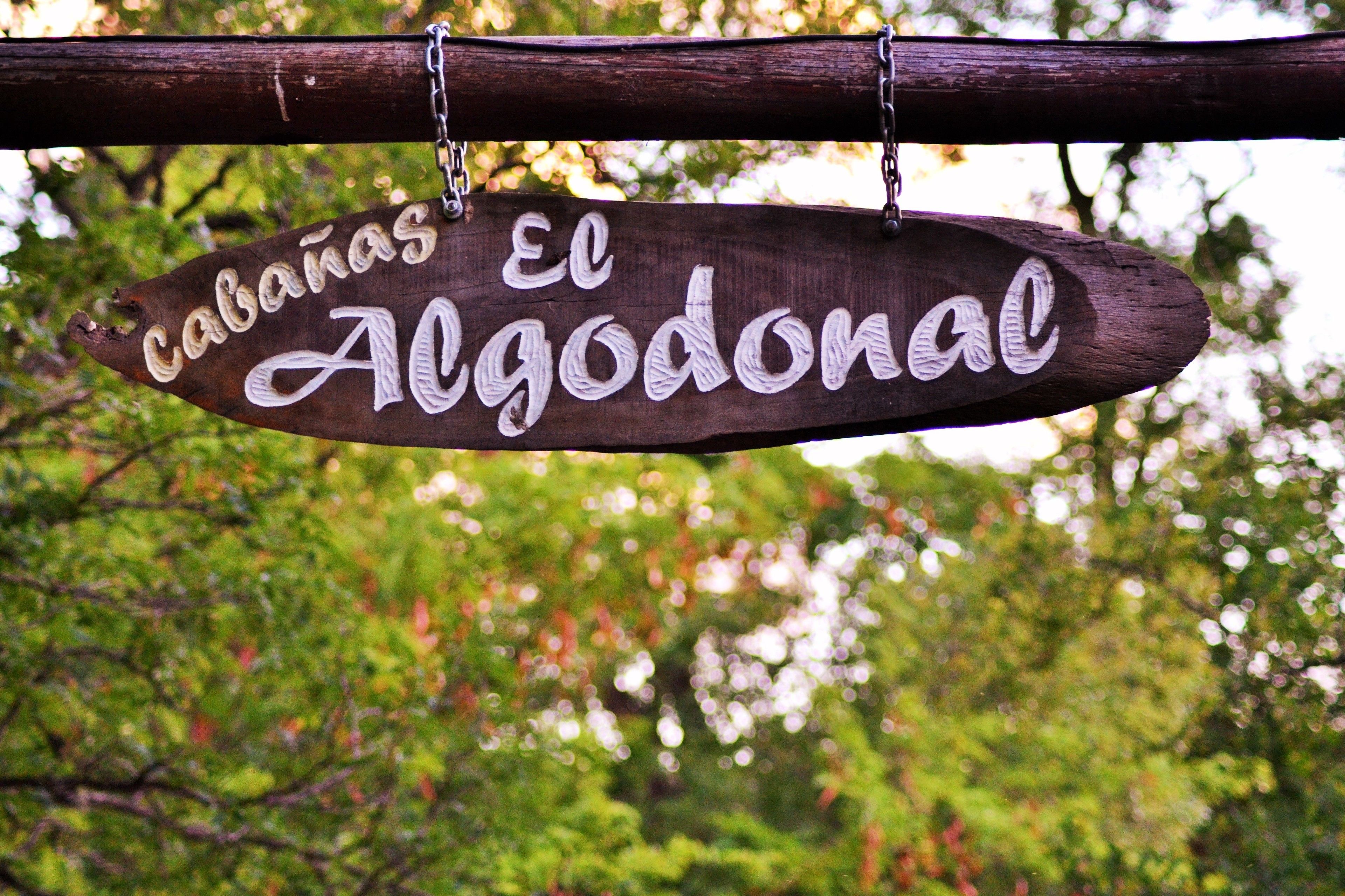 A wooden sign with the text "Cabanas El Algodonal" hanging from a wooden post.