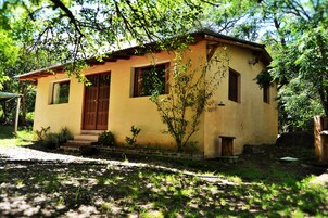 A small, single-story building with a yellow facade, a wooden door, and windows with shutters.