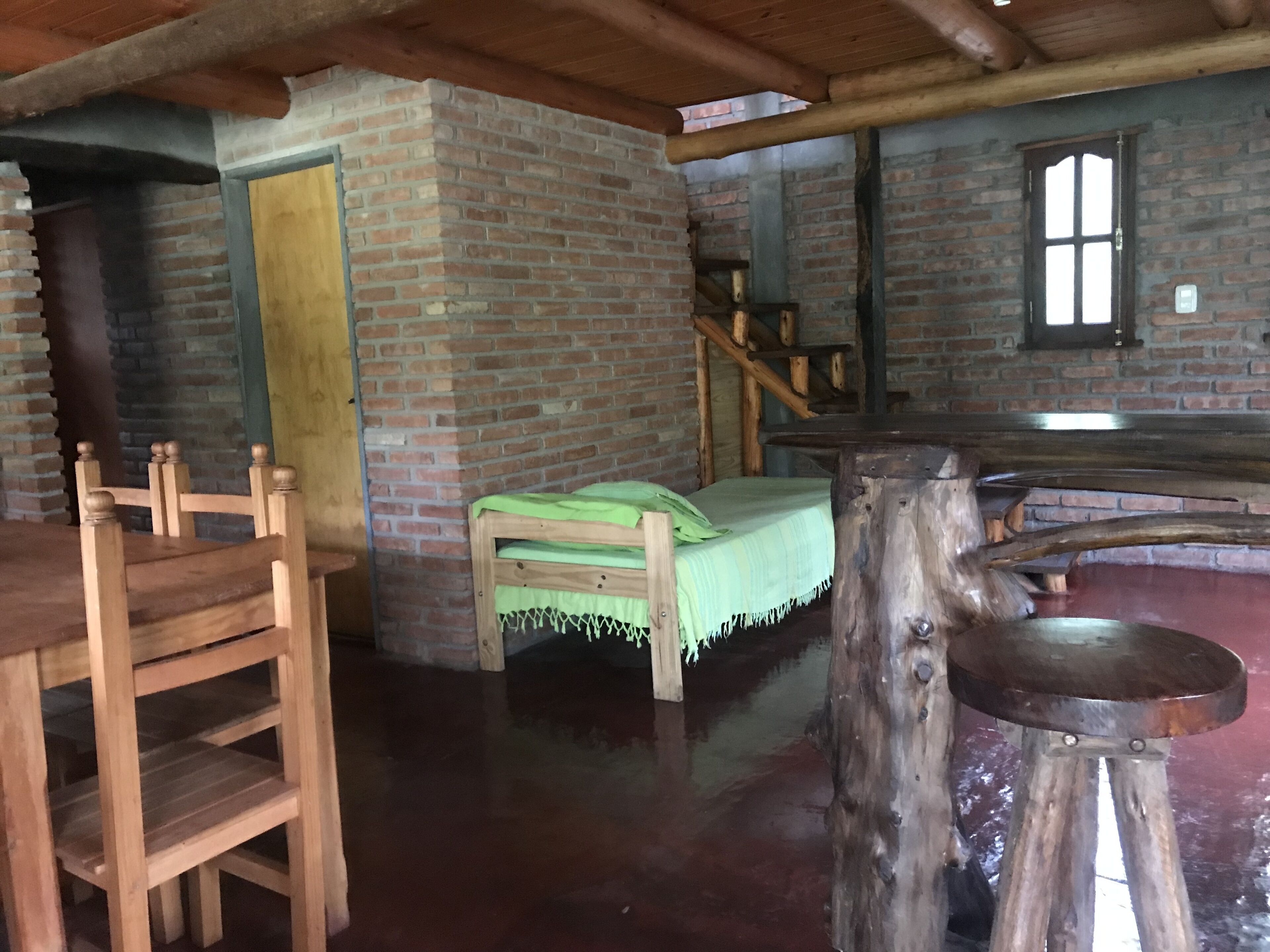 Una habitación rústica con una cama, una silla, una mesa y una escalera de madera, así como una pared de ladrillo.
