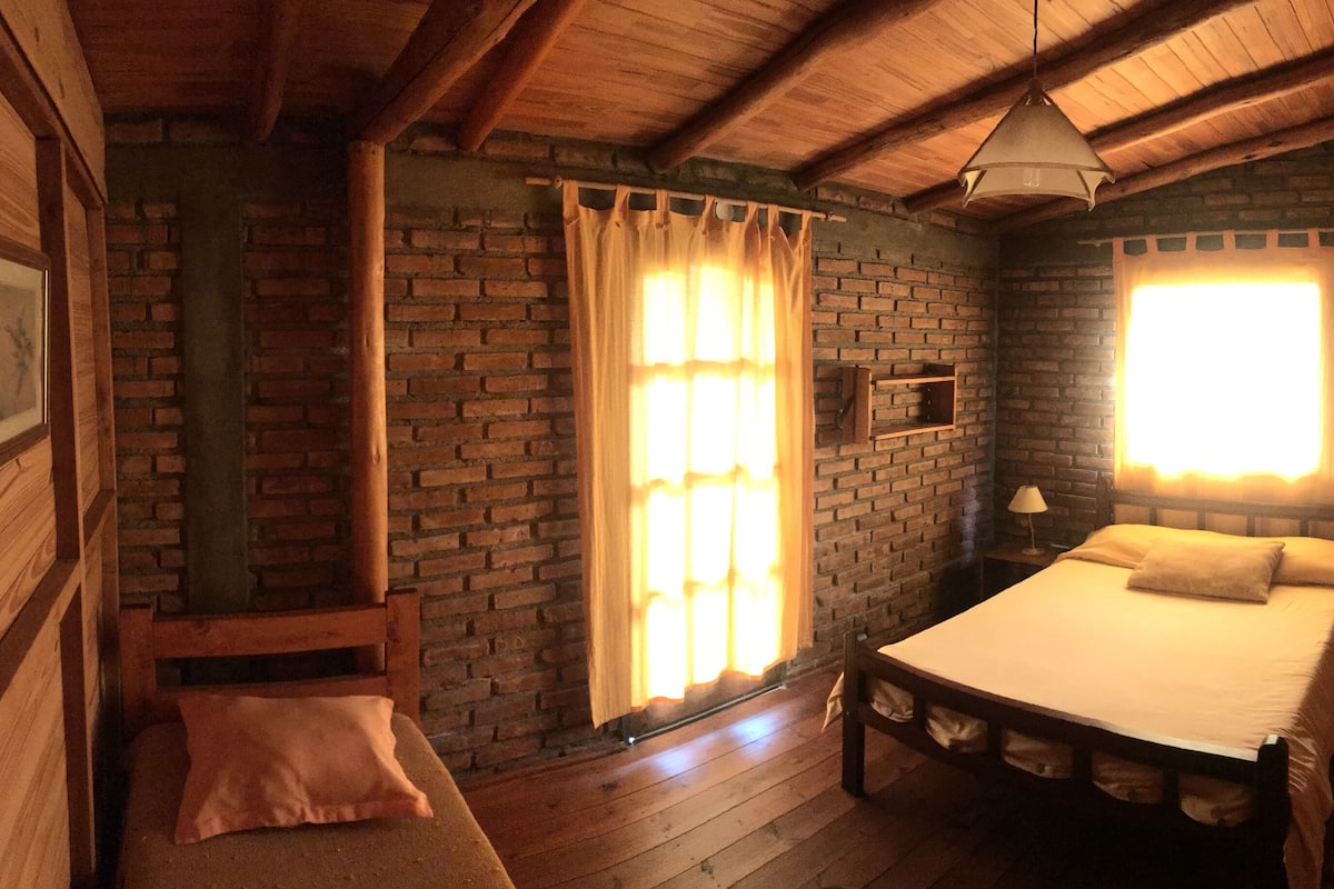 A cozy room with a wooden bed, a bench, and a brick wall.