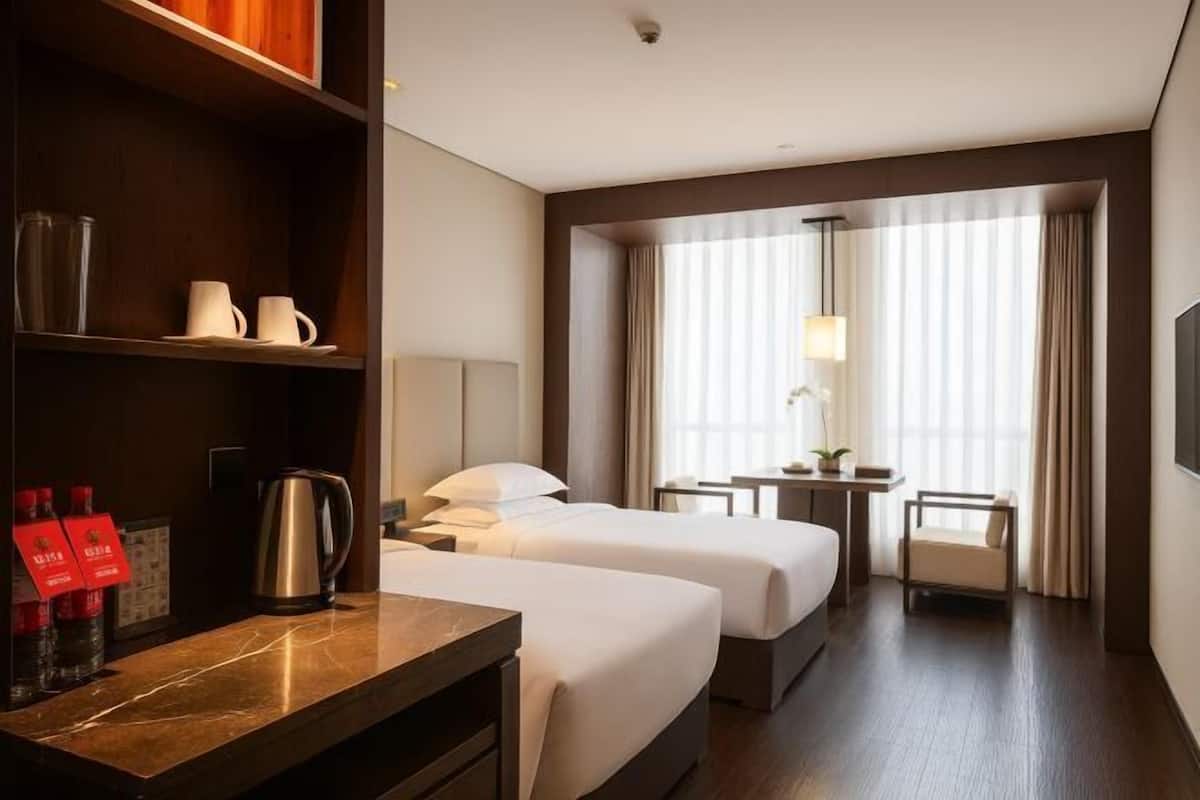 Habitación de hotel con dos camas, un escritorio, cafetera, lámpara, silla y televisor.