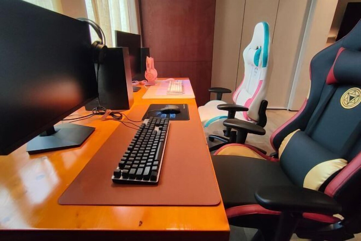 A wooden desk with a computer setup including a monitor, keyboard, and mouse. There is a gaming chair and a mouse pad.