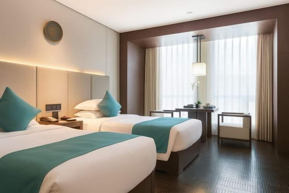 Habitación de hotel con dos camas, un escritorio, una silla y un ventanal con cortinas.