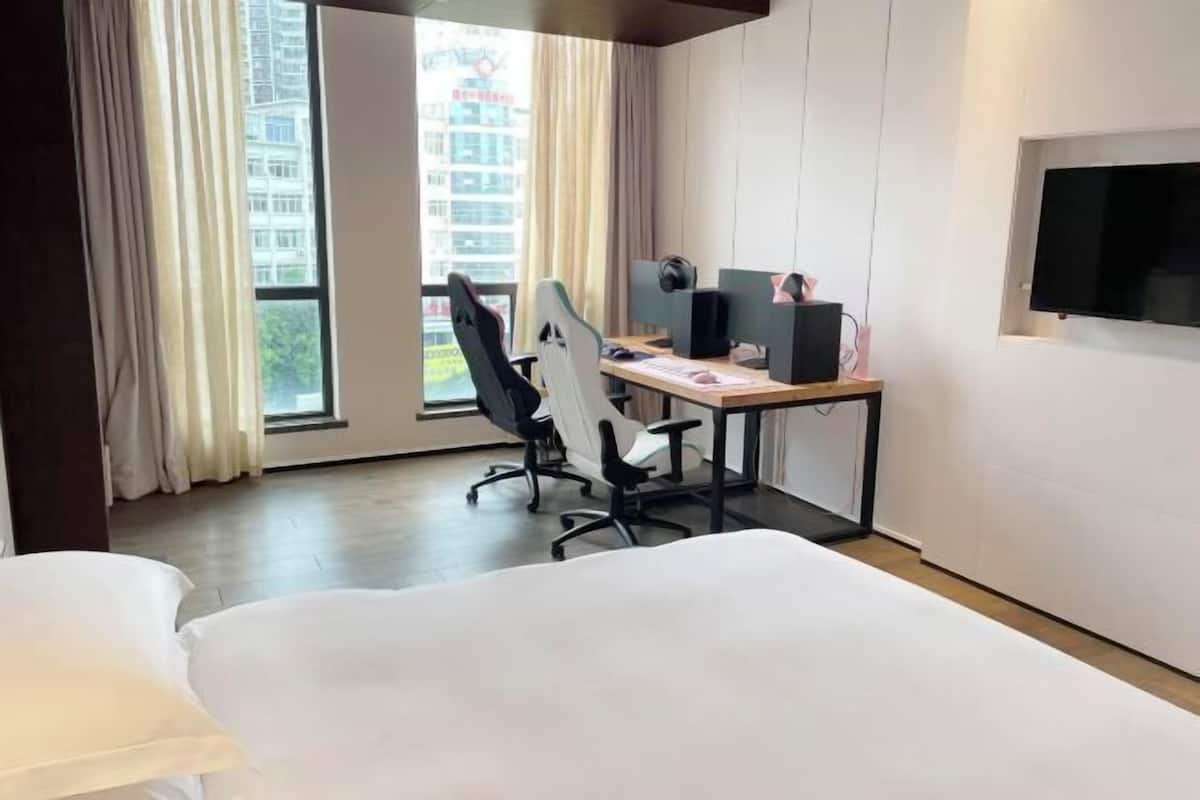 Habitación de hotel con cama, escritorio con computadora, silla, televisor y ventana con cortinas.