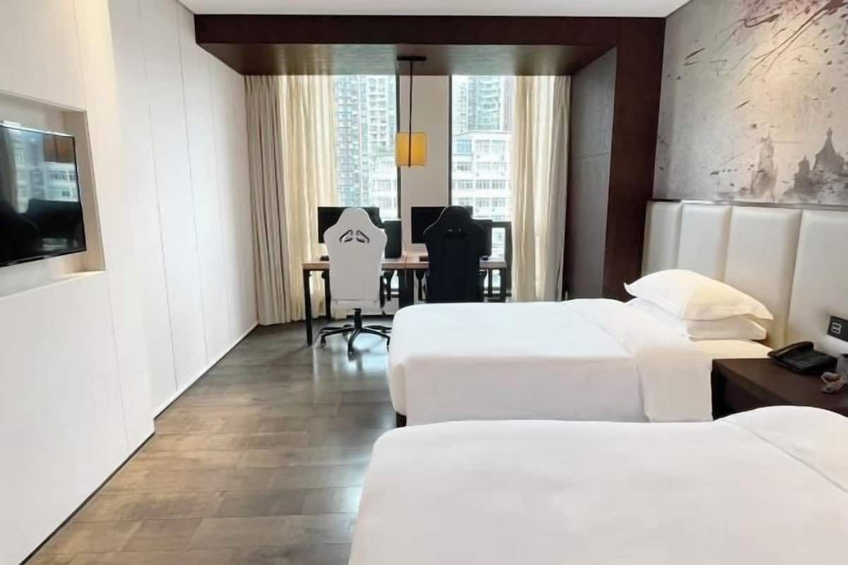 Habitación de hotel con dos camas, un escritorio con silla, televisor y vista a la ciudad.