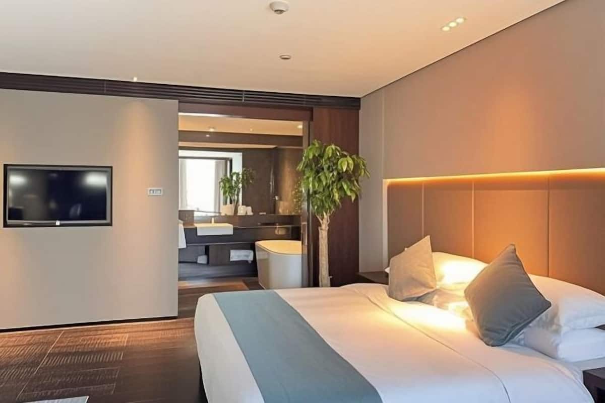 Una habitación de hotel moderna con cama, mesita de noche, televisor y baño visible a través de una puerta abierta.